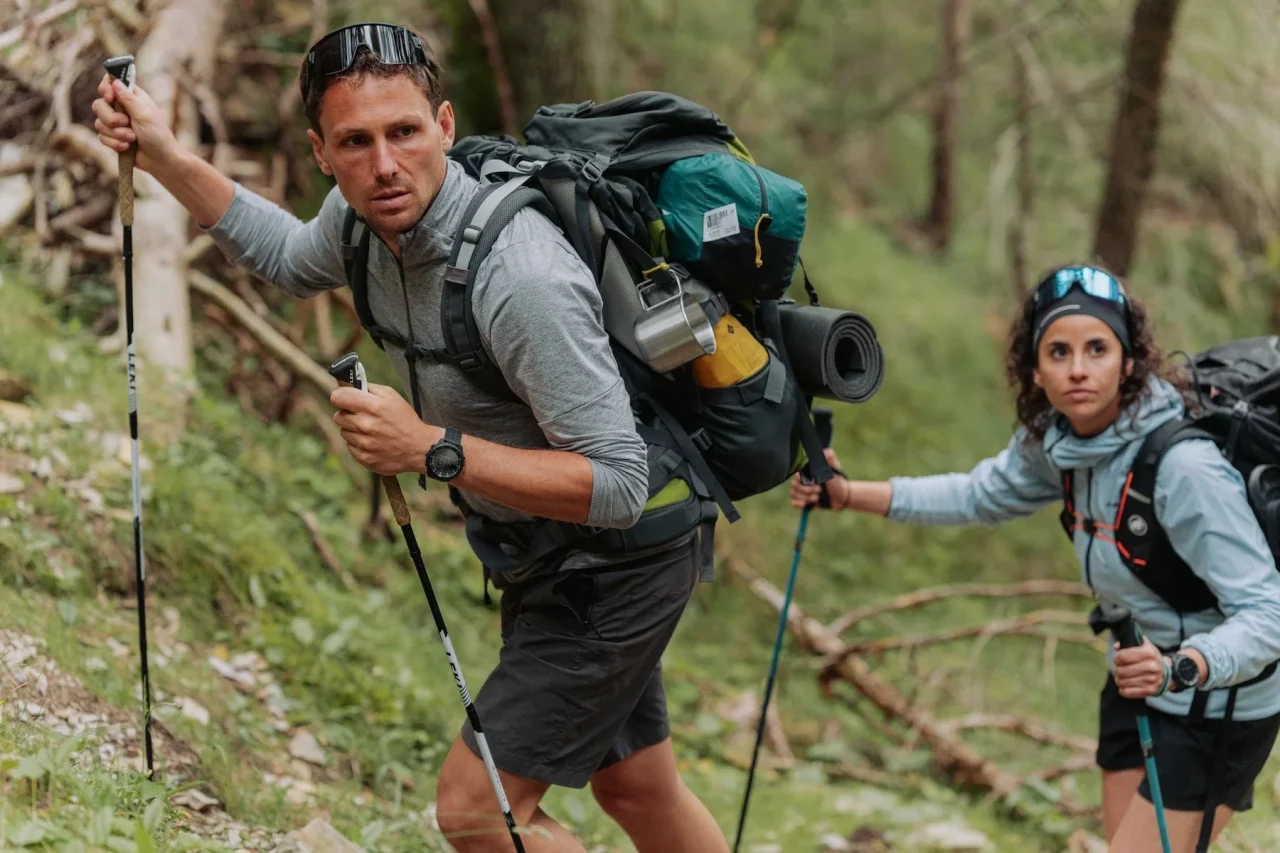 トレッキングポールを持ち登山する男女。男性は腕時計を着用