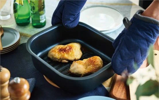 GRISIAのグリル調理で焼き色がついた鶏もも肉2枚を、ミトンで持つ黒い角型容器