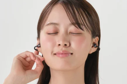 目を閉じ耳にイヤホンを着けて片手で耳元に触れる女性