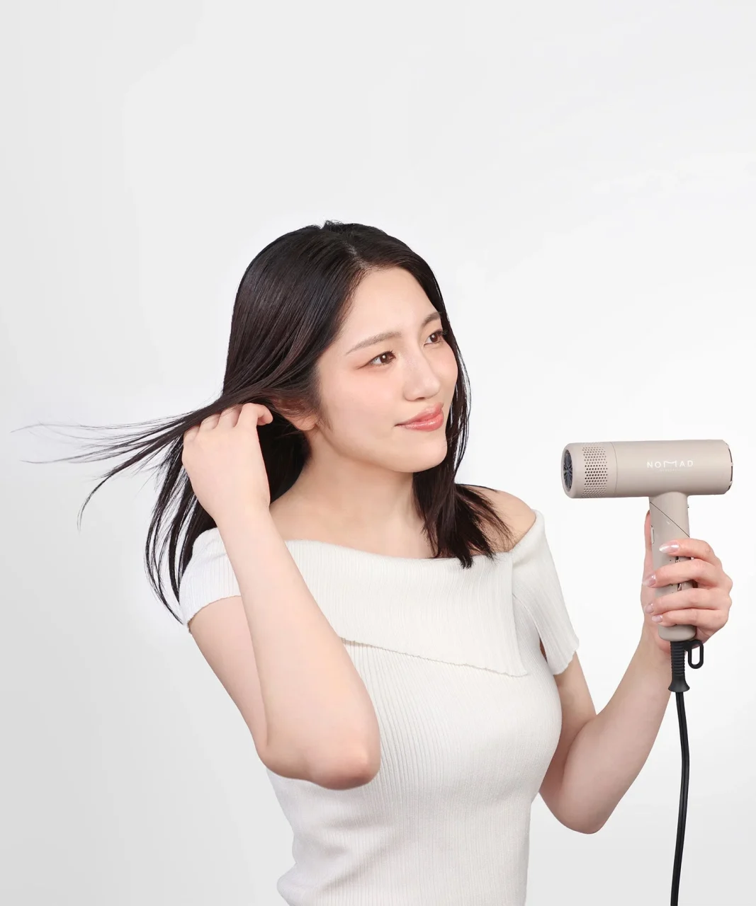 ベージュ系のドライヤーで髪を乾かす黒髪の女性