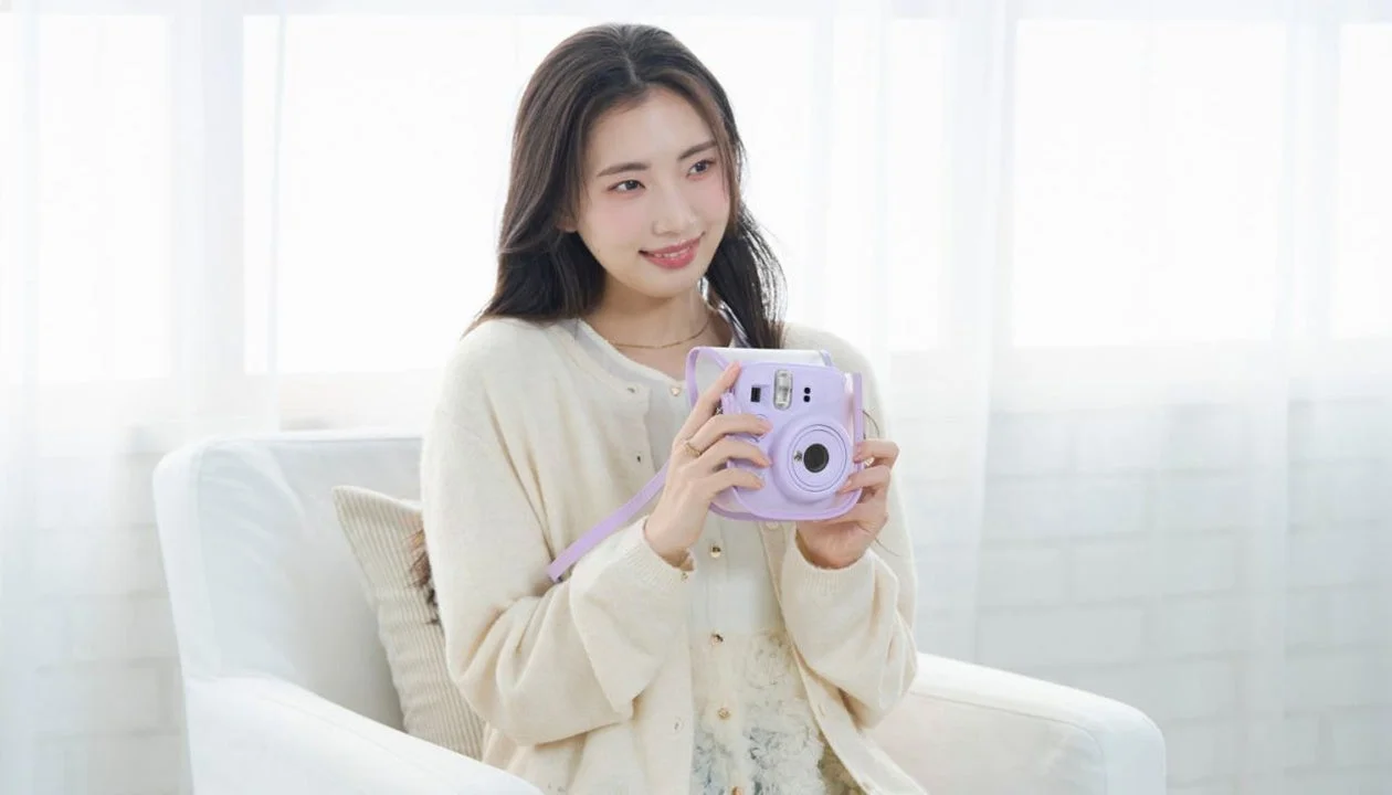 淡いパープルのチェキを両手で持つ、白いカーディガン姿の女性