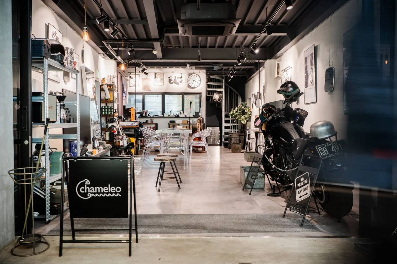 黒い看板とバイクが置かれた、スツールやテーブルのあるカフェ店内