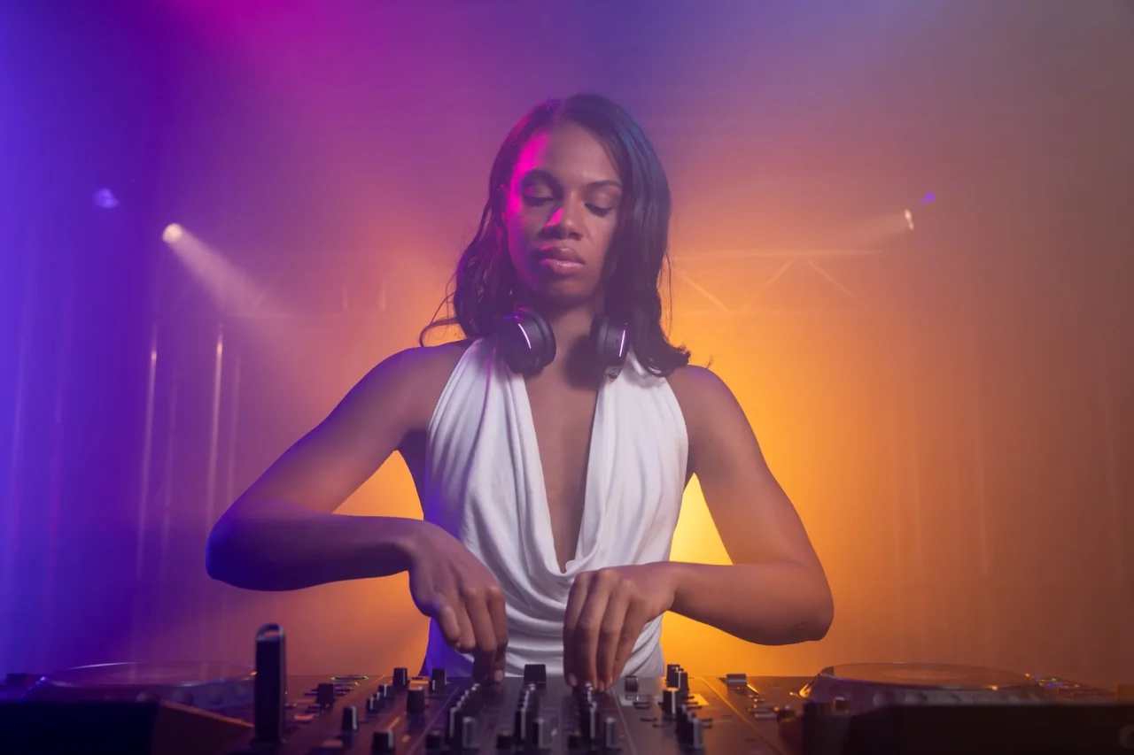 カラフルな照明の中、首にヘッドホンをかけてDJ機器を操作する女性