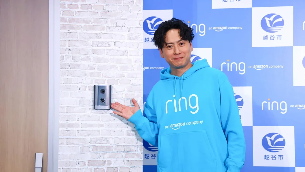 ringのパーカーの男性が壁のRing 防犯ドアホン プロを手で示す