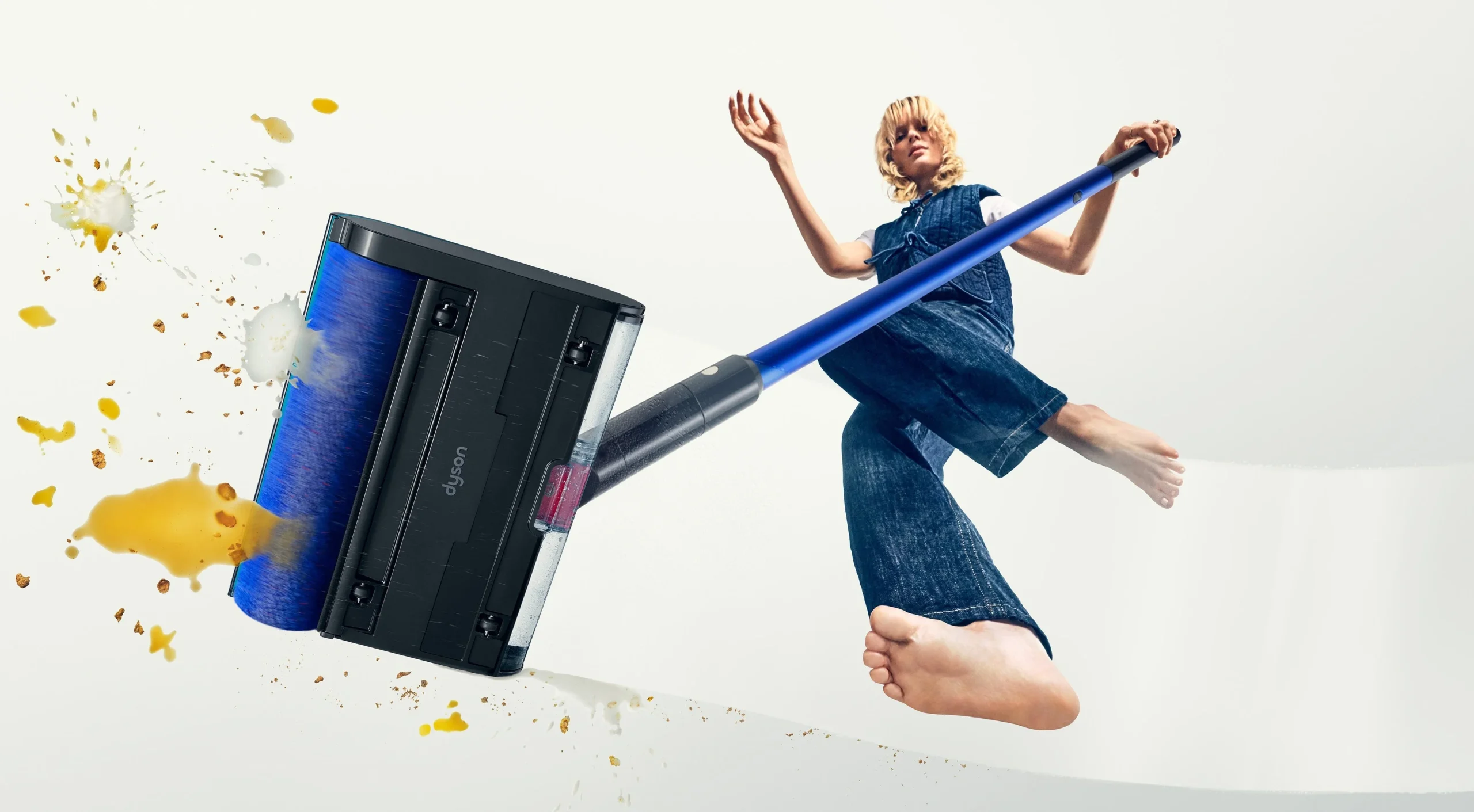 Dyson W1 PencilWash+Dok™の青いローラーヘッドと、汚れが飛び散る中で操作する人物