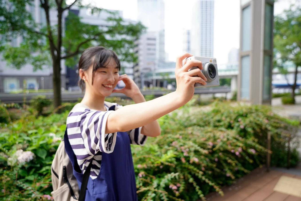 屋外でカメラを自分に向けて自撮りする縞模様の服の女性(セルフィー専用レンズ)