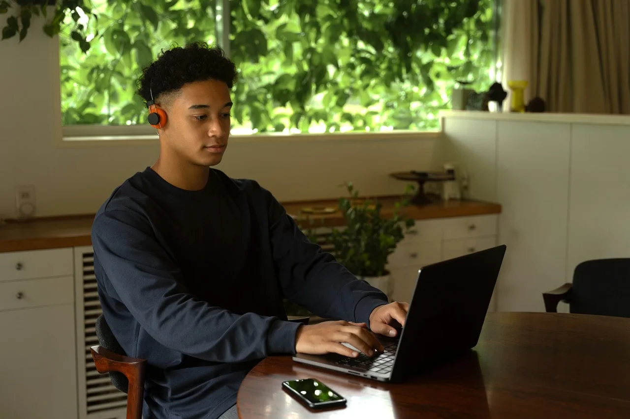 オレンジのヘッドホンを着け、ノートPCを操作する男性