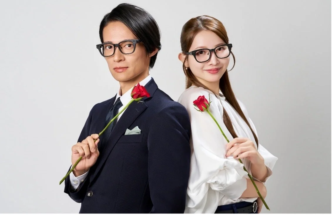 黒縁眼鏡をかけ赤いバラを持つ背中合わせのスーツ姿の男性と白いブラウスの女性