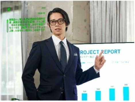 眼鏡をかけ視界に緑の文字が表示された、スーツ姿の男性のプレゼン風景