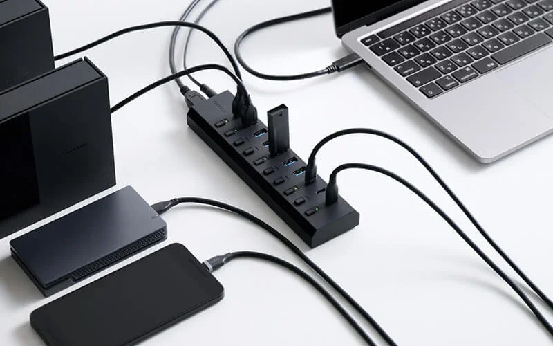 多くのUSB機器を接続した黒い10ポートUSBハブとノートPC