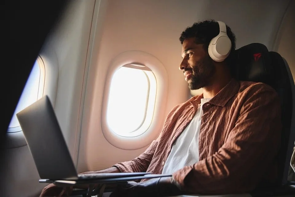 機内の窓際でヘッドホンをつけノートPCを使う男性