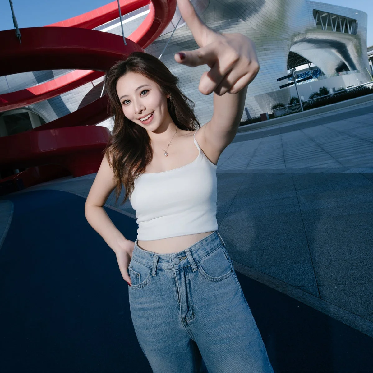 赤い曲線の構造物と建物を背景に、指を差し出す白いトップスの女性