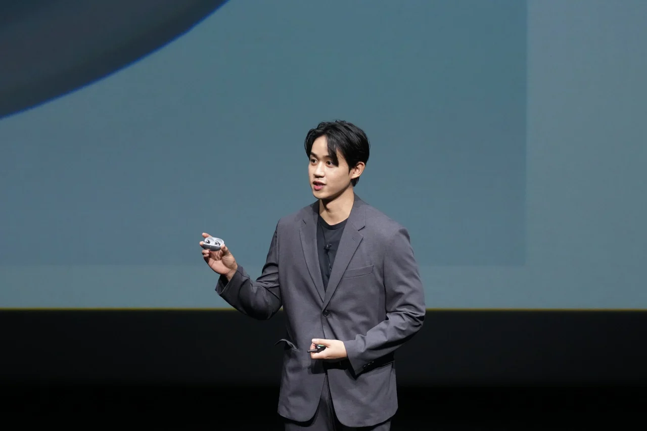 HUAWEI FreeBuds Neoを手に持ち、登壇して説明するグレーのスーツの男性