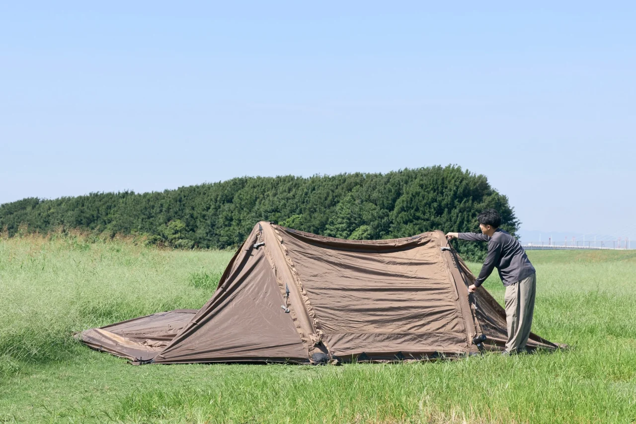 草地でエアテントの設営作業をする人。茶色のテントを広げている