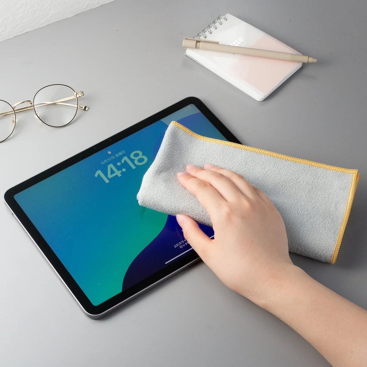 グレーのマイクロファイバー生地でタブレット画面を拭く手