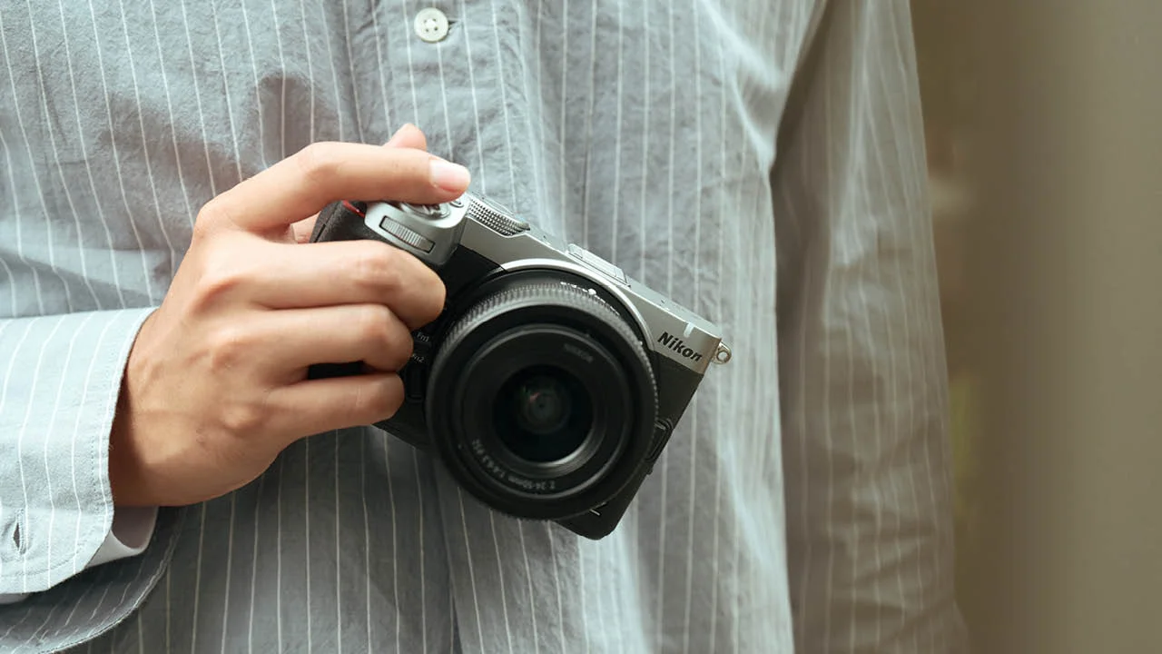 ストライプシャツの人物が片手でNikonのカメラを持つ様子