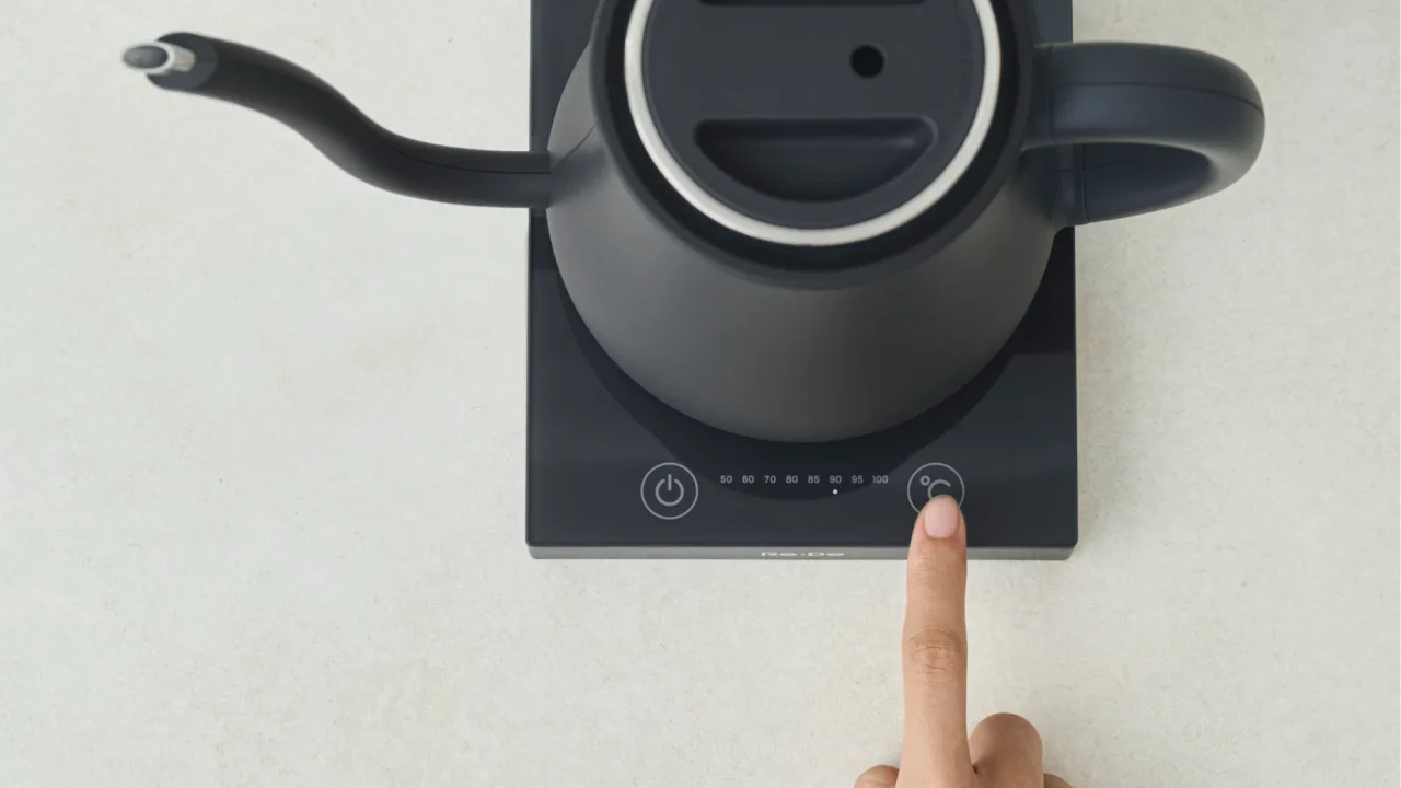 電源プレート上の黒いケトルと温度表示の操作ボタンを押す指