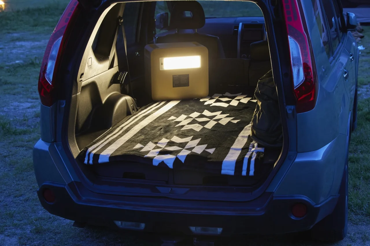 夕暮れの車の荷室に敷物と光るポータブル電源が置かれている様子