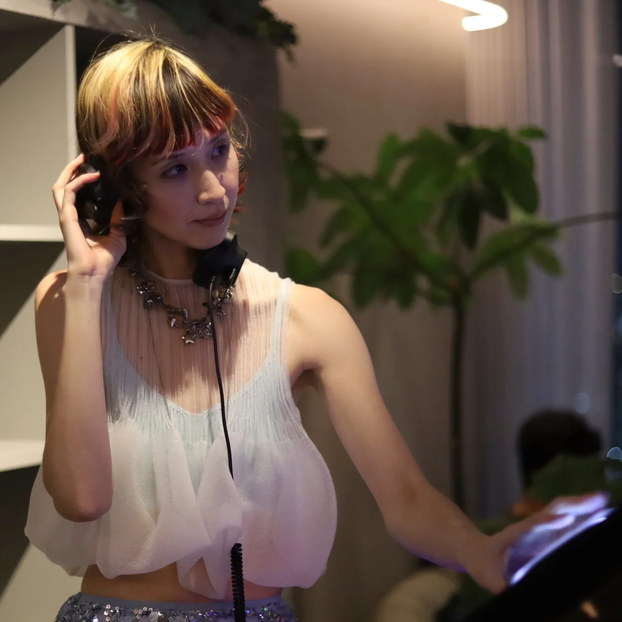 ヘッドホンを片耳に当ててDJプレイする白いトップスの女性