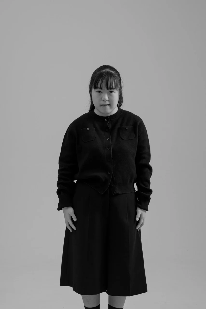 作家marinaのモノクロポートレート。黒いカーディガンとスカートで立つ姿