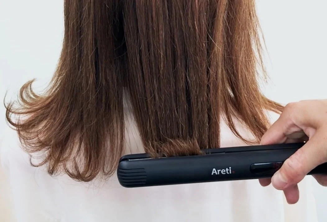 黒いAreti.のストレートアイロンで茶髪の毛先を挟んでいる様子