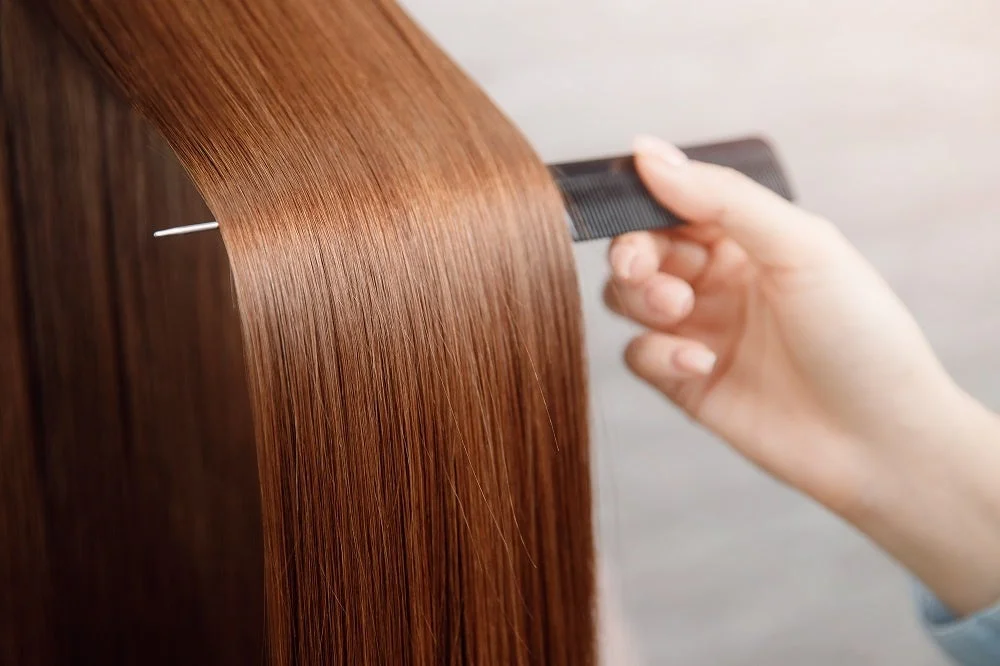 茶色のつややかなストレートヘアにコームを当てる手元