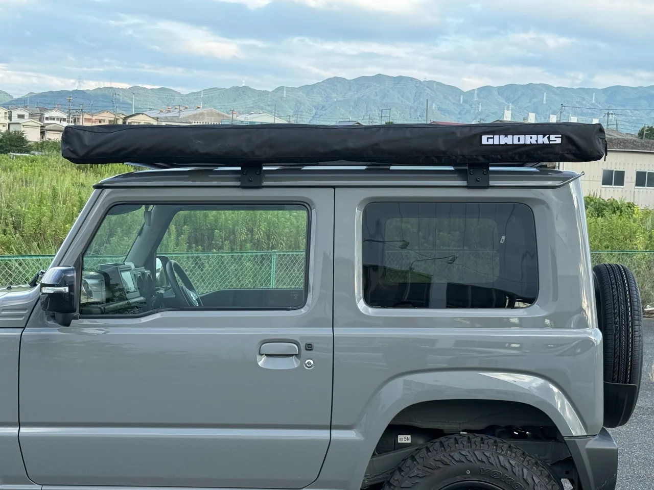 グレーのジムニー屋根に装着したGIWORKSの黒い収納状態のオーニング