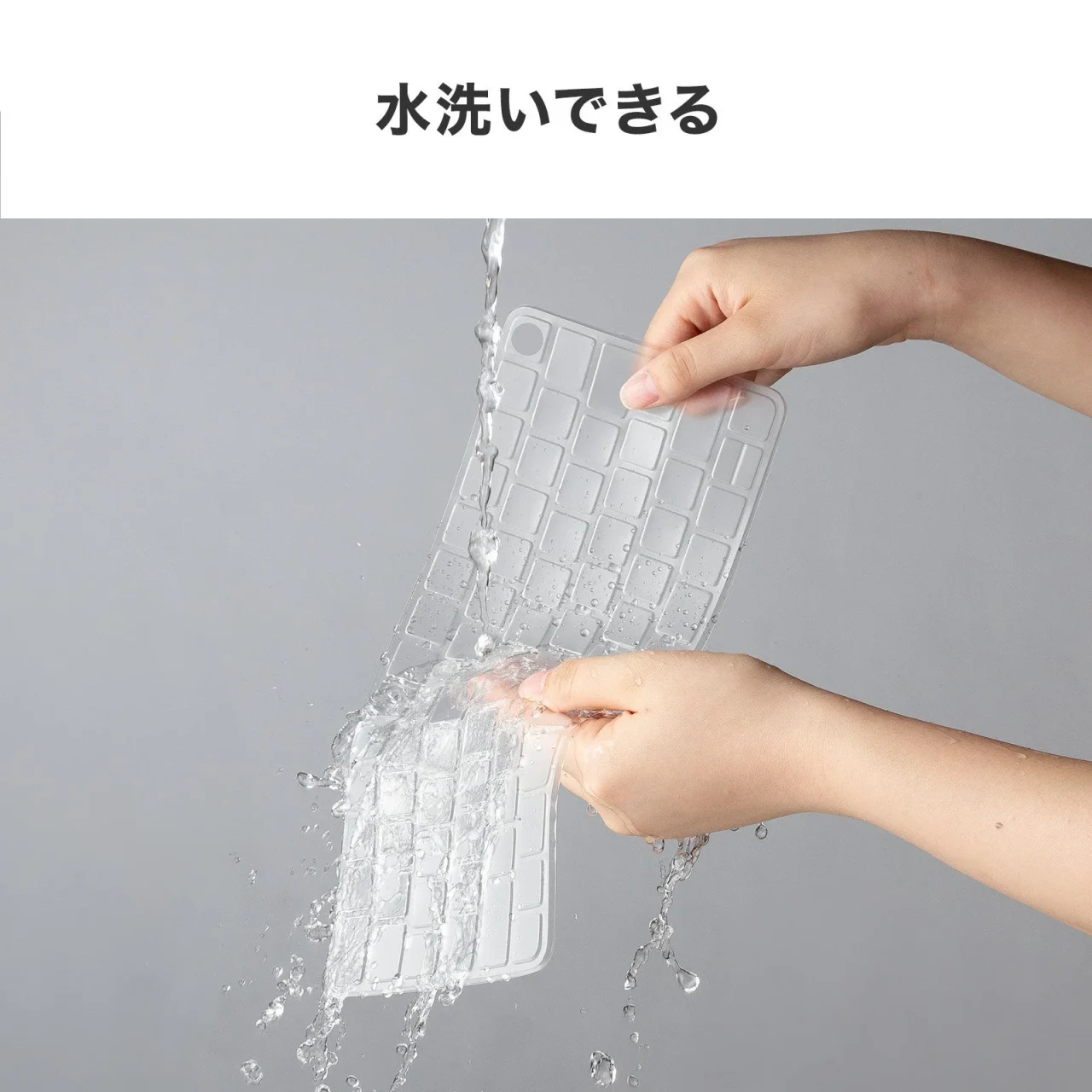 透明なキーボードカバーを両手で持ち、水で洗う様子