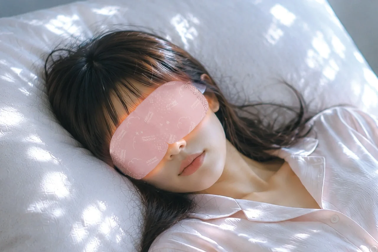 ピンク色のあたためアイウォーマーを目元に着けて横になる女性