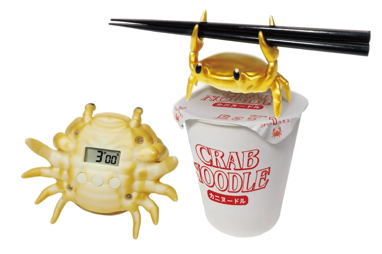 黄金のカニ型カップラーメンタイマー。カップ麺の上で箸を持つ金色のカニと表示付き本体