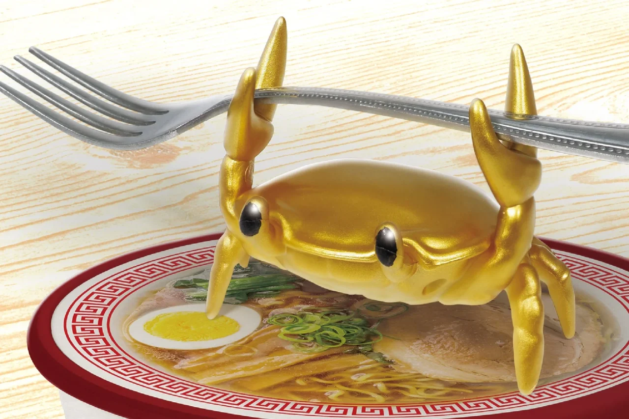 黄金のカニ型カップラーメンタイマーがフォークを挟みカップ麺に乗る様子