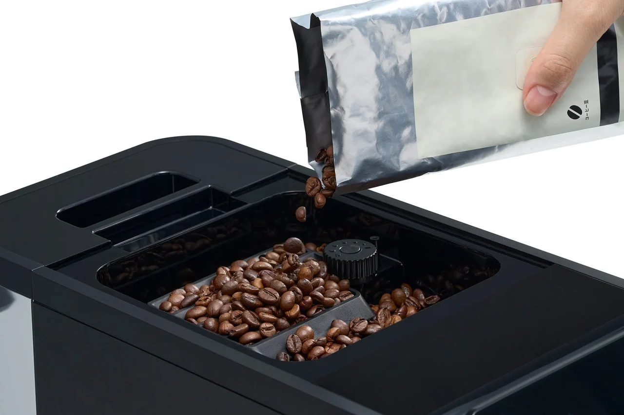 ホッパーにコーヒー豆の袋から豆を入れる様子。約280g入るホッパー容量