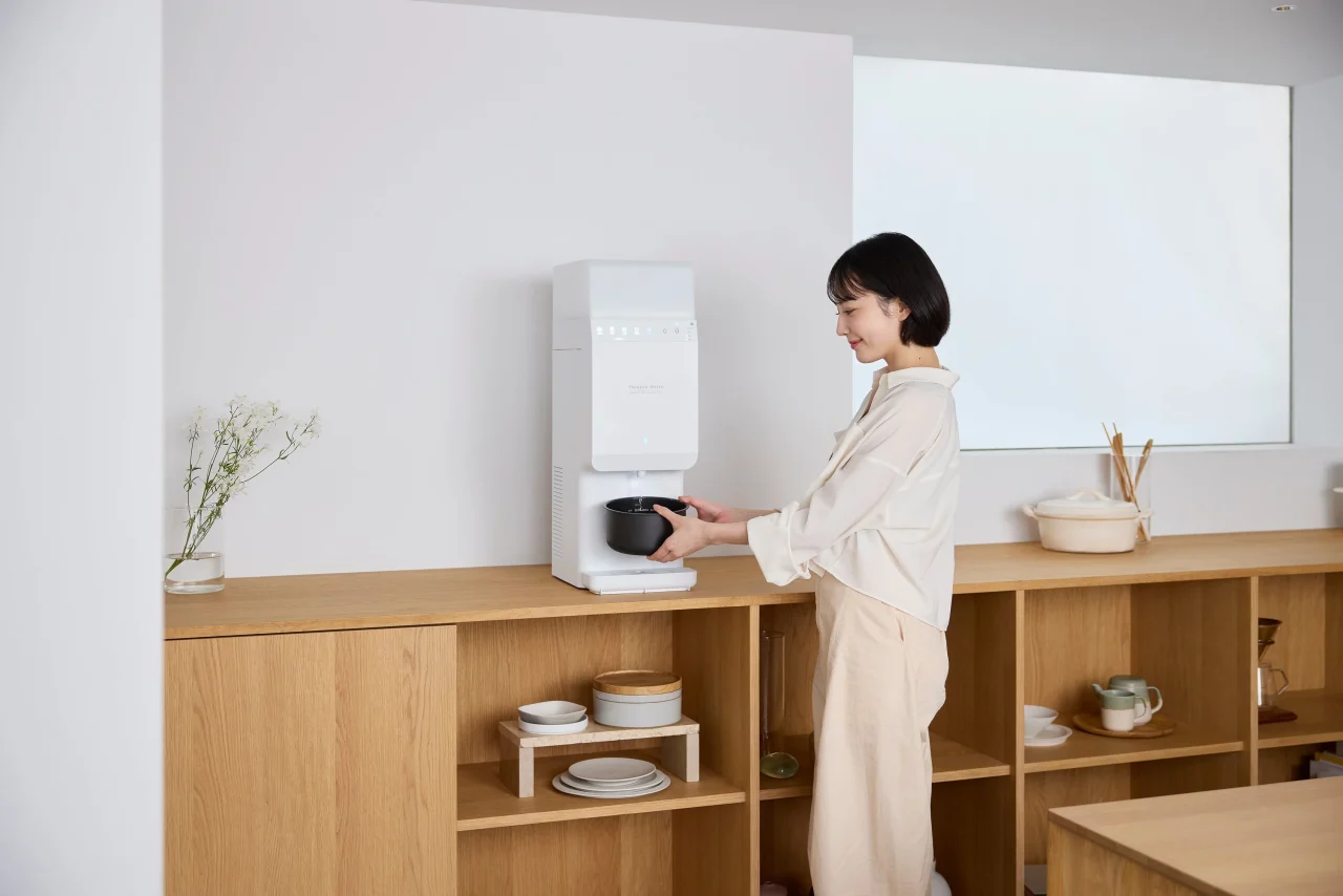 利用イメージ：木製棚の前で白いサーバーにカップをセットする女性