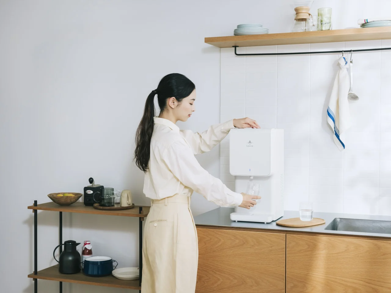キッチンで白いウォーターサーバーからコップに水を注ぐ女性の利用イメージ