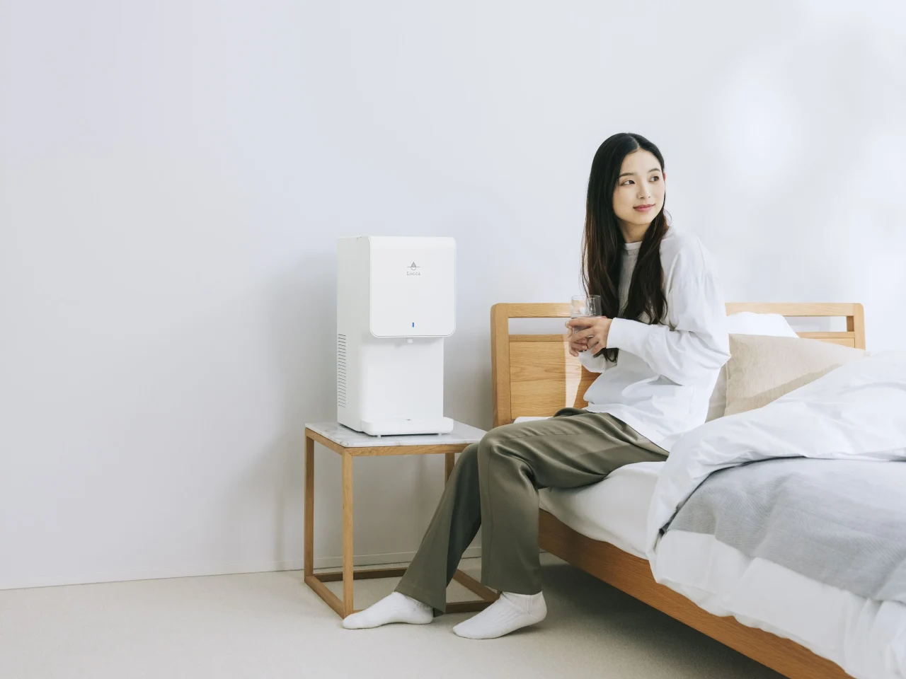 利用イメージ:ベッドに座る女性と、サイドテーブル上の白いウォーターサーバー