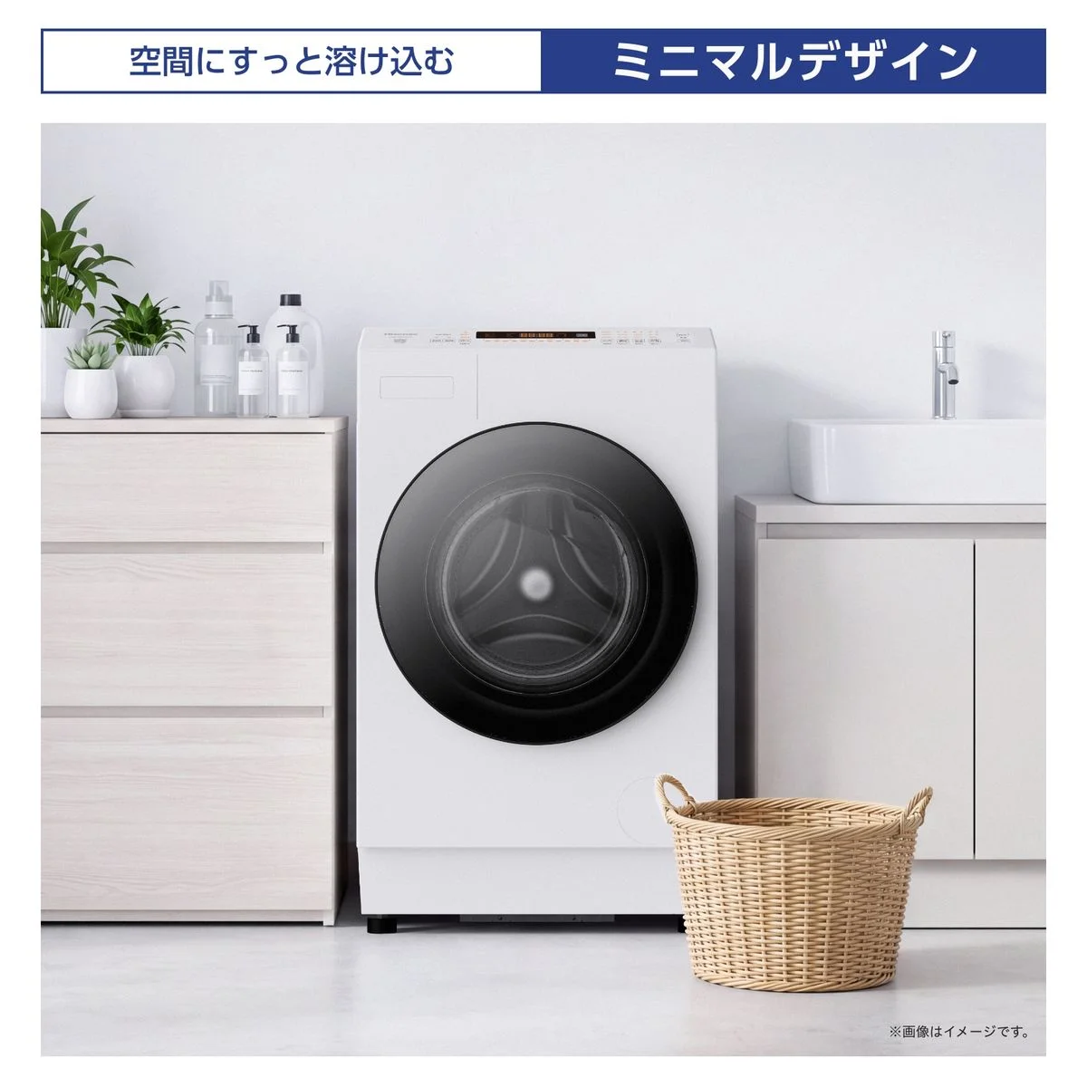 白いドラム式洗濯乾燥機と脚元のかご、洗面台のある空間