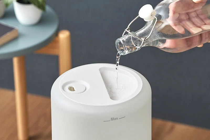 上部給水タイプの加湿器に、ガラス瓶から上の給水口へ水を注ぐ様子