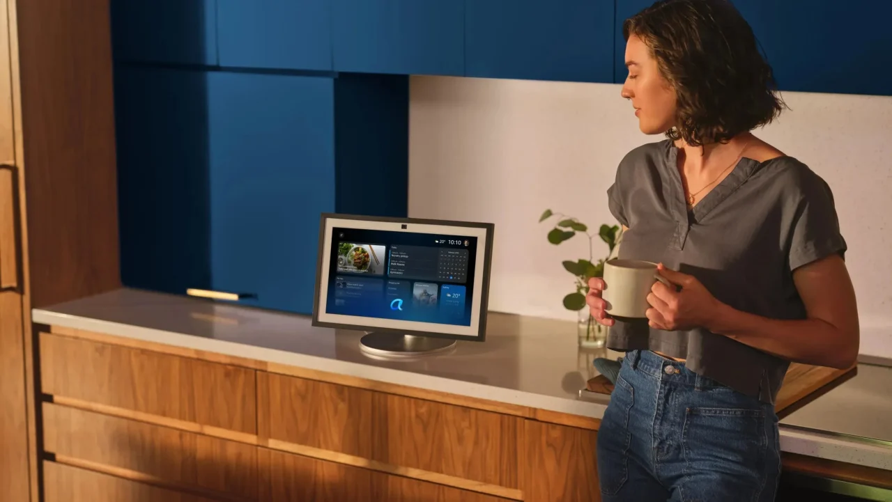 キッチンでスクリーン端末を見ながらマグカップを持つ女性。Alexa+の利用シーン