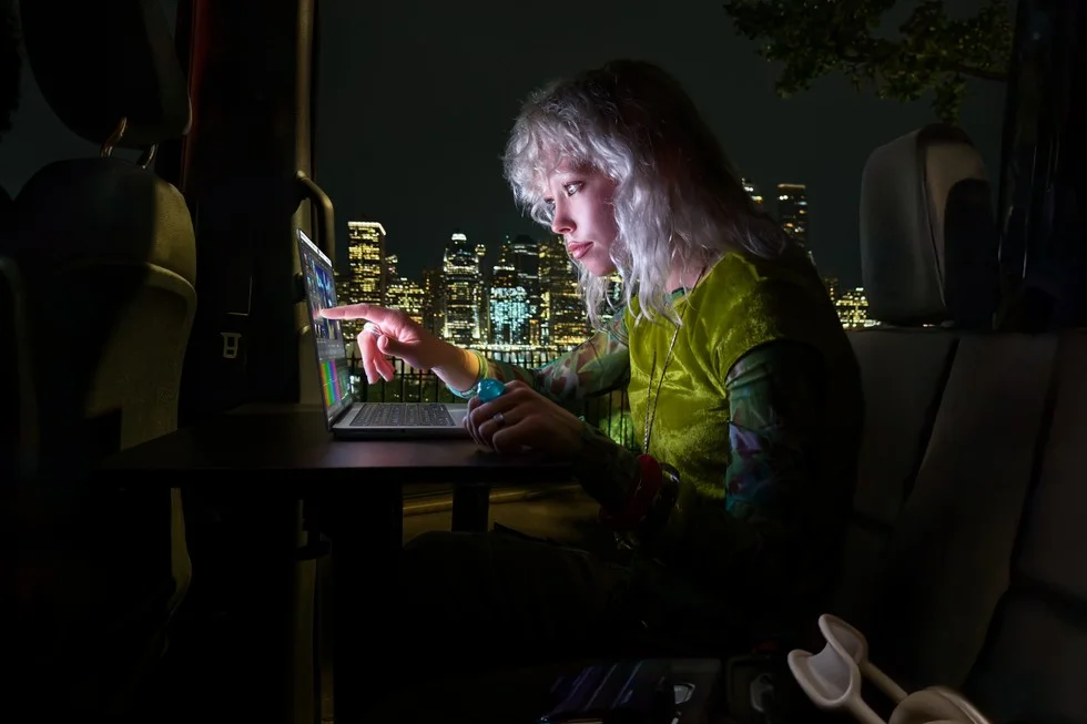 夜景を背にノートパソコンの画面に指で触れる、緑の服の人物