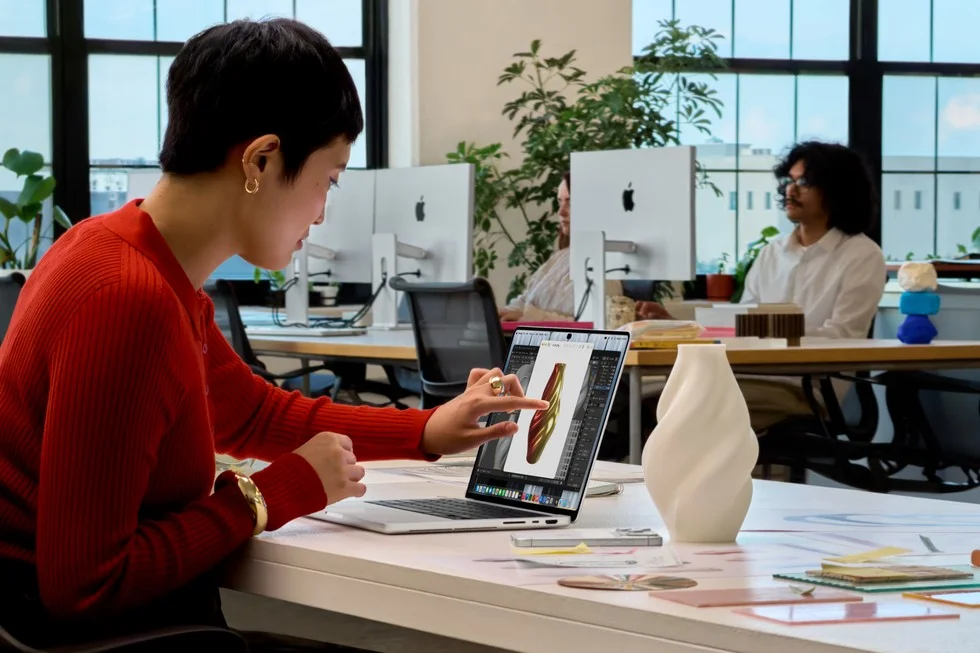 オフィスでMacBook Proの画面にタッチ操作する赤いセーターの人物