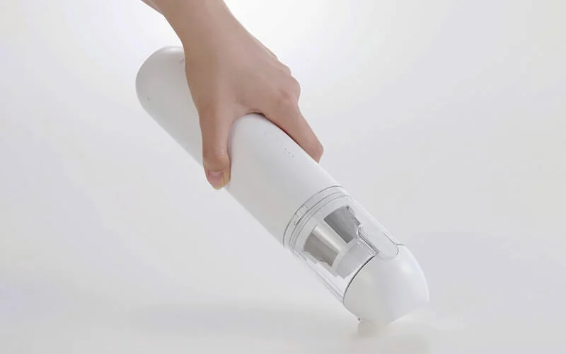 片手で握って床のゴミを吸引する白いコードレスハンディクリーナー