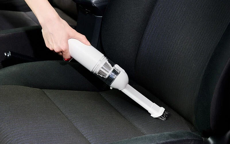 車のシートを掃除する白いコードレスハンディクリーナー